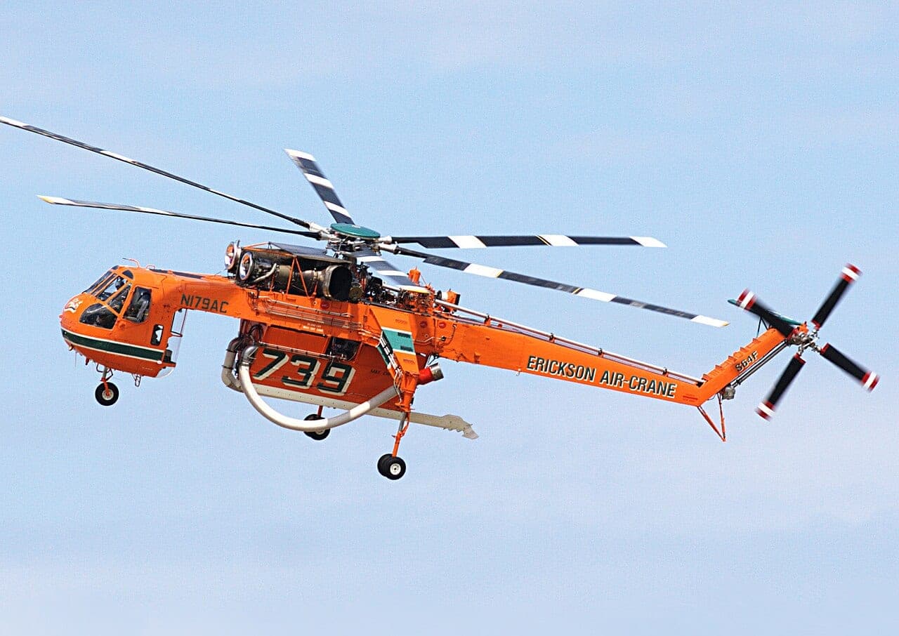 Orange Erickson S-64 Aircrane helitanker in flight with its water tank and snorkel visible